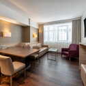 Ein modernes Hotelzimmer mit einem Sitzbereich, Tisch, Stühlen und einem Fernseher, erhellt von natürlichem Licht.