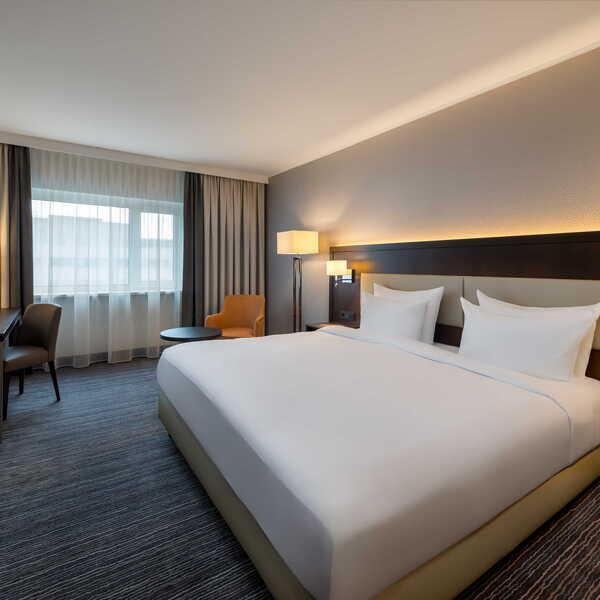 A modern hotel room featuring a double bed, desk, and ample natural light from the window. | © Name