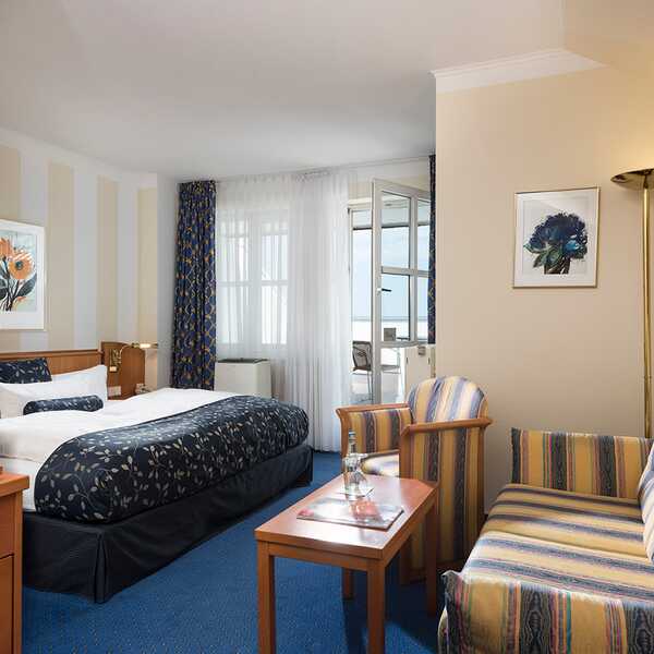 Ein elegantes Hotelzimmer mit einem gemütlichen Sitzbereich, einem Bett und einer Kaffeemaschine auf einem Holztisch.