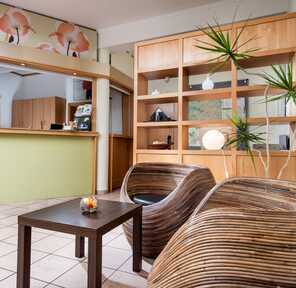 A modern lobby features stylish wicker chairs, a wooden coffee table, and a vibrant floral mural enhancing the decor.