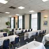 A well-lit meeting room features rows of tables and chairs set up for a conference with a projection screen at the front.