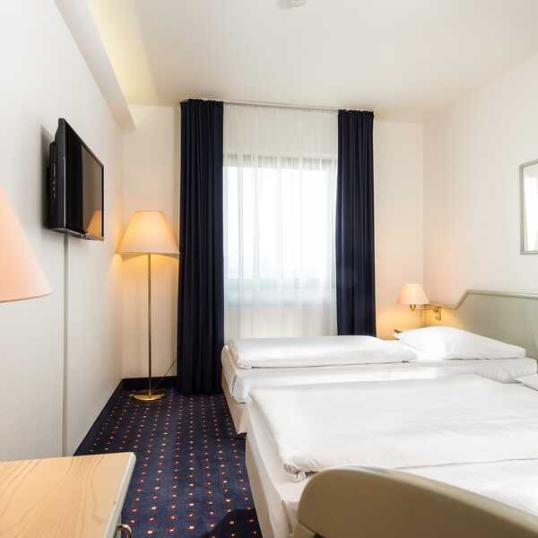 Ein helles Zweibettzimmer mit zwei Einzelbetten, einem Fernseher und gemütlicher Beleuchtung lädt zum Entspannen ein.