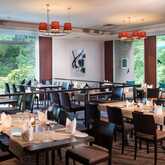 A modern restaurant interior features neatly set tables and large windows overlooking lush greenery.