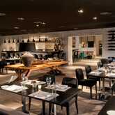 A modern restaurant with elegant black chairs and tables is set for dining, featuring ambient lighting and contemporary decor.