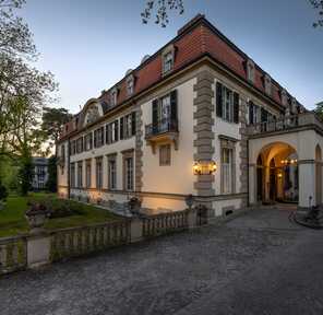 Die elegante Fassade eines historischen Hotels, umgeben von Bäumen im Abendlicht.
