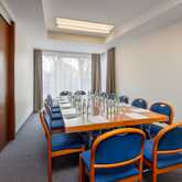 A conference room with a long wooden table is set up with blue chairs, water bottles, and paper under soft lighting.