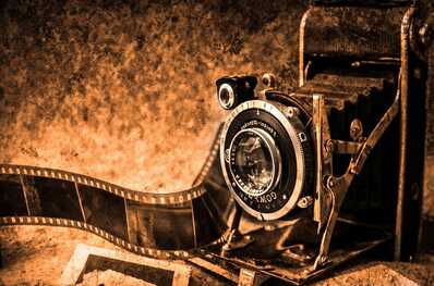 A vintage folding camera rests beside a roll of film, evoking a nostalgic atmosphere in a sepia-toned setting.