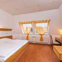 A cozy double room features a neatly made bed, warm lighting, and a TV, with orange curtains accentuating the windows.