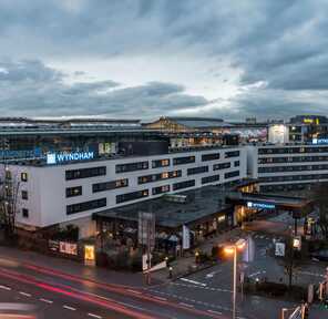 A bustling evening scene shows the exterior of the Wyndham Hotel near ICS, with traffic lights illuminating the street.