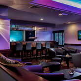 Hotelbar mit stilvollen Sesseln, einem beleuchteten Tresen und einem Fernseher im Hintergrund.