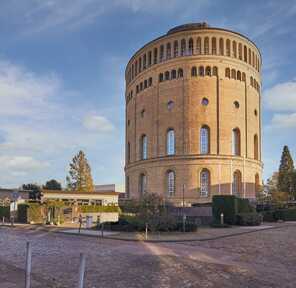 The historic Wasserturm in Cologne stands tall under a clear blue sky, surrounded by cobblestone streets and greenery.