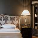 Die Executive Suite zeigt ein elegantes Bett mit verziertem Kopfteil, daneben ein stilvoller Nachttisch mit Lampe.