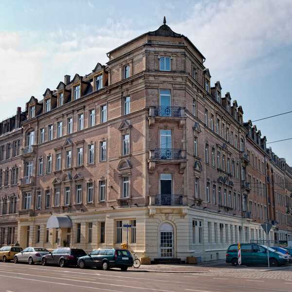 Historic brick building on a city corner with parked cars lining the street under a clear sky.