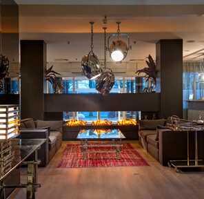 A modern hotel lobby features sleek sofas, a vibrant red rug, and a striking fireplace centerpiece for a welcoming ambiance.