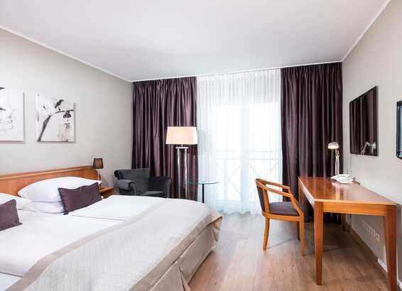A modern double room features a cozy bed, a work desk, and elegant decor with soft lighting and dark curtains.