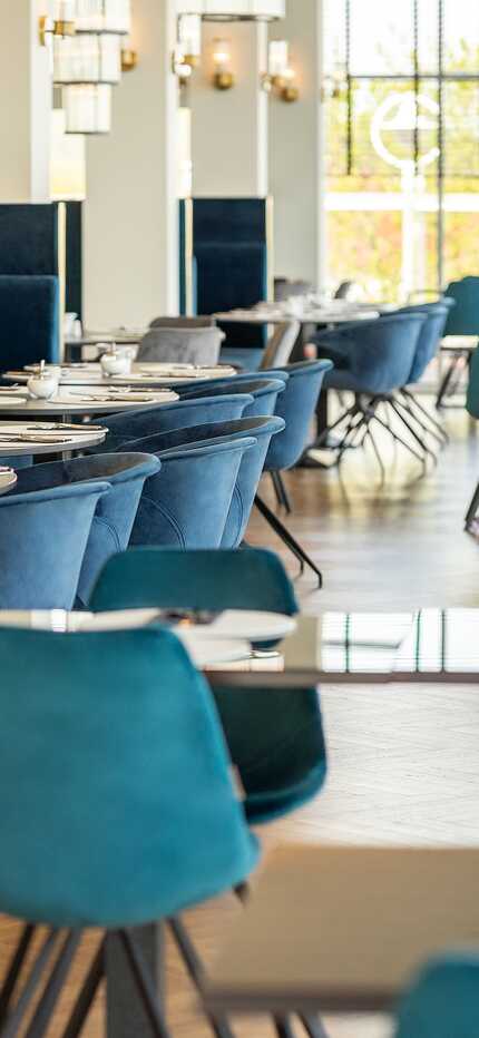Ein elegantes Frühstücksrestaurant mit blauen Samtstühlen und gedeckten Tischen wartet auf Gäste.