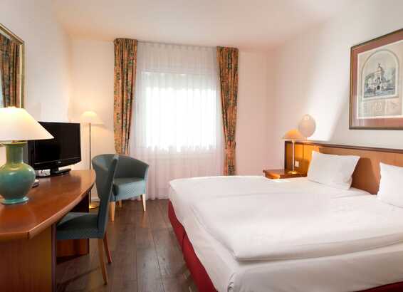 Ein gemütliches Doppelzimmer mit einem großen Bett, einem Schreibtisch, einem Fernseher und geschmackvoller Einrichtung.