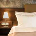 A cozy deluxe room features a neatly made bed with plush pillows and a bedside lamp on a wooden nightstand.