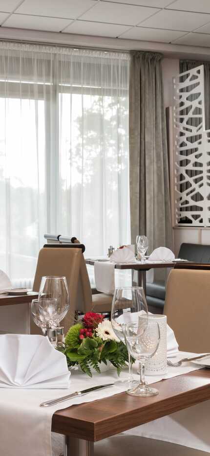 Ein elegantes Restaurant mit gedeckten Tischen, stilvollen Stühlen und floralen Dekorationen lädt zum Genießen ein.