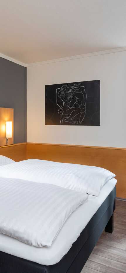 A modern standard room features a neatly made bed, stylish artwork, and a cozy seating area by the window.