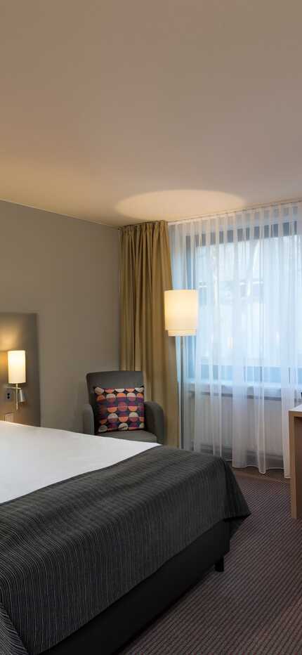 A cozy single room features a neatly made bed, a desk by the window, and modern decor, creating a comfortable standard setup.