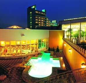 The illuminated hotel exterior at night features a glowing pool and vibrant indoor lounge area.