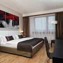 A modern double room features a stylish bed, artwork, and a desk with a TV, creating a comfortable and elegant space.