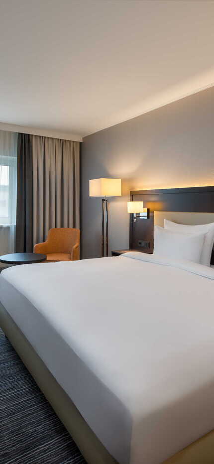 Modernes Hotelzimmer mit Doppelbett, Schreibtisch und gemütlichem Stuhl bei Tageslicht | © Name