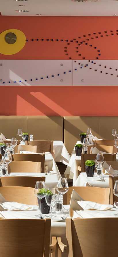 The modern restaurant interior features neatly set tables with white tablecloths and a vibrant orange wall design.