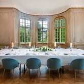 A luxurious dining room features a long, elegantly set table with blue chairs and ornate chandeliers illuminating the space.