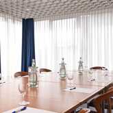 A modern conference room with a large wooden table, set with water bottles, glasses, and notepads, is ready for a meeting.
