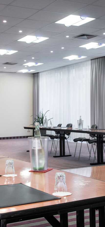 A modern conference room with a U-shaped table setup, ready for a meeting with notepads and water bottles.