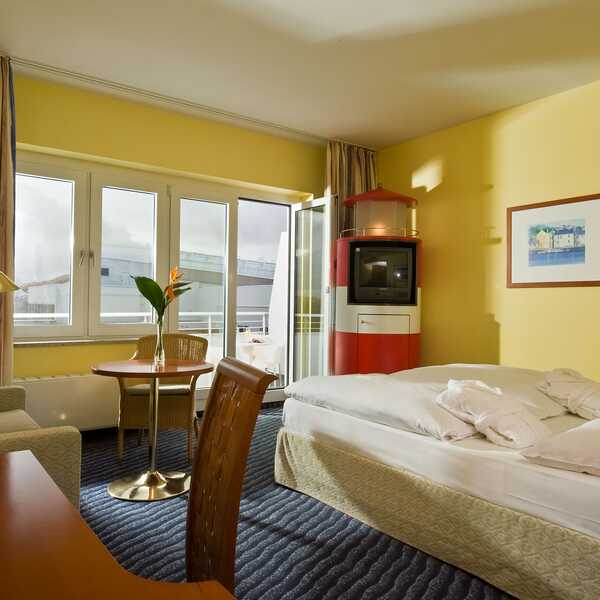 Ein gemütliches Standardzimmer mit gelben Wänden, einem Doppelbett, Schreibtisch und einem kleinen Tisch am Fenster.