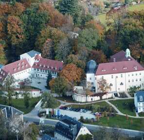 Luftaufnahme eines großen Gebäudekomplexes umgeben von herbstlich verfärbtem Wald in einer idyllischen Landschaft.