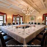 An elegant conference room with a U-shaped table setup, adorned with red curtains and a chandelier.