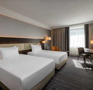 Helles Hotelzimmer mit zwei Einzelbetten, einem Schreibtisch und großen Fenstern | © Name