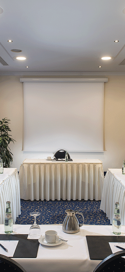 Ein heller, professioneller Konferenzraum mit U-förmigem Tisch, vorbereitet für ein Meeting mit Notizblöcken und Getränken.
