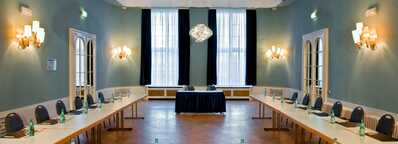 A conference room with a U-shaped table arrangement is set up for a meeting, featuring water bottles and notepads.