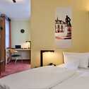 A modern business room features a cozy bed, a work desk with a laptop, and a stylish decor on the wall.