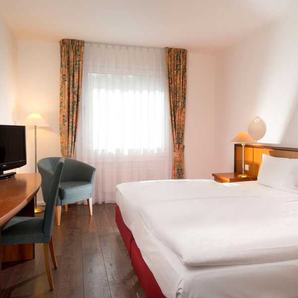 Ein gemütliches Doppelzimmer mit einem großen Bett, einem Schreibtisch, einem Fernseher und geschmackvoller Einrichtung.