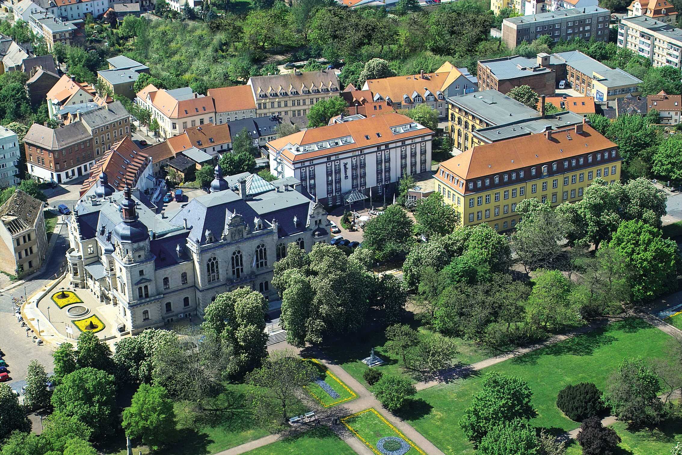 Luftbild zeigt ein charmantes Hotel umgeben von grünen Bäumen und historischen Gebäuden in einer städtischen Umgebung.