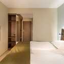 A cozy double room features a neatly made bed, wall-mounted TV, and open wardrobe, exuding a warm and inviting ambiance.