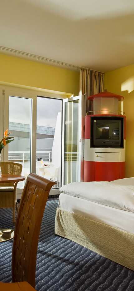 A cozy standard room features a neatly made bed, a small dining table, and a vintage TV cabinet, all under soft lighting.