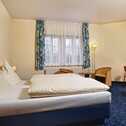 A cozy double room features a neatly made bed, wooden furniture, and a window with floral curtains.