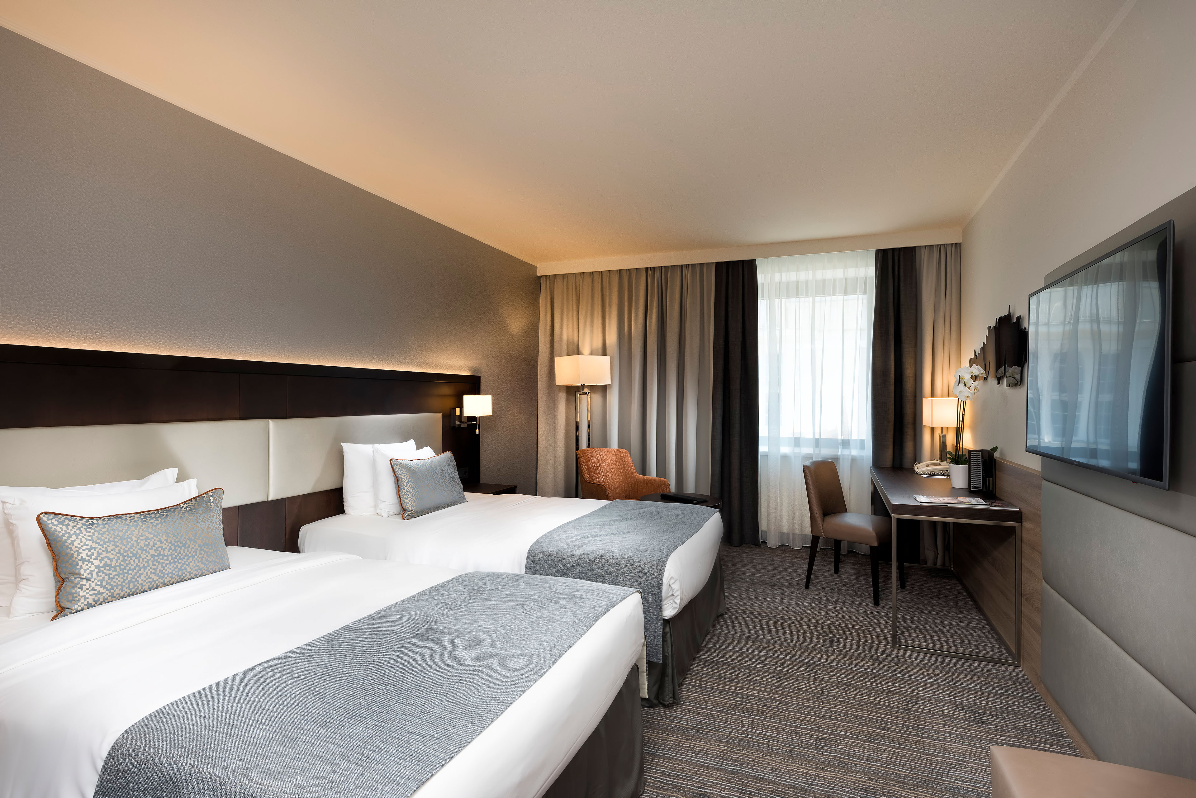 Zwei komfortable Einzelbetten stehen in einem modern eingerichteten Zimmer mit Schreibtisch und großem Fenster.